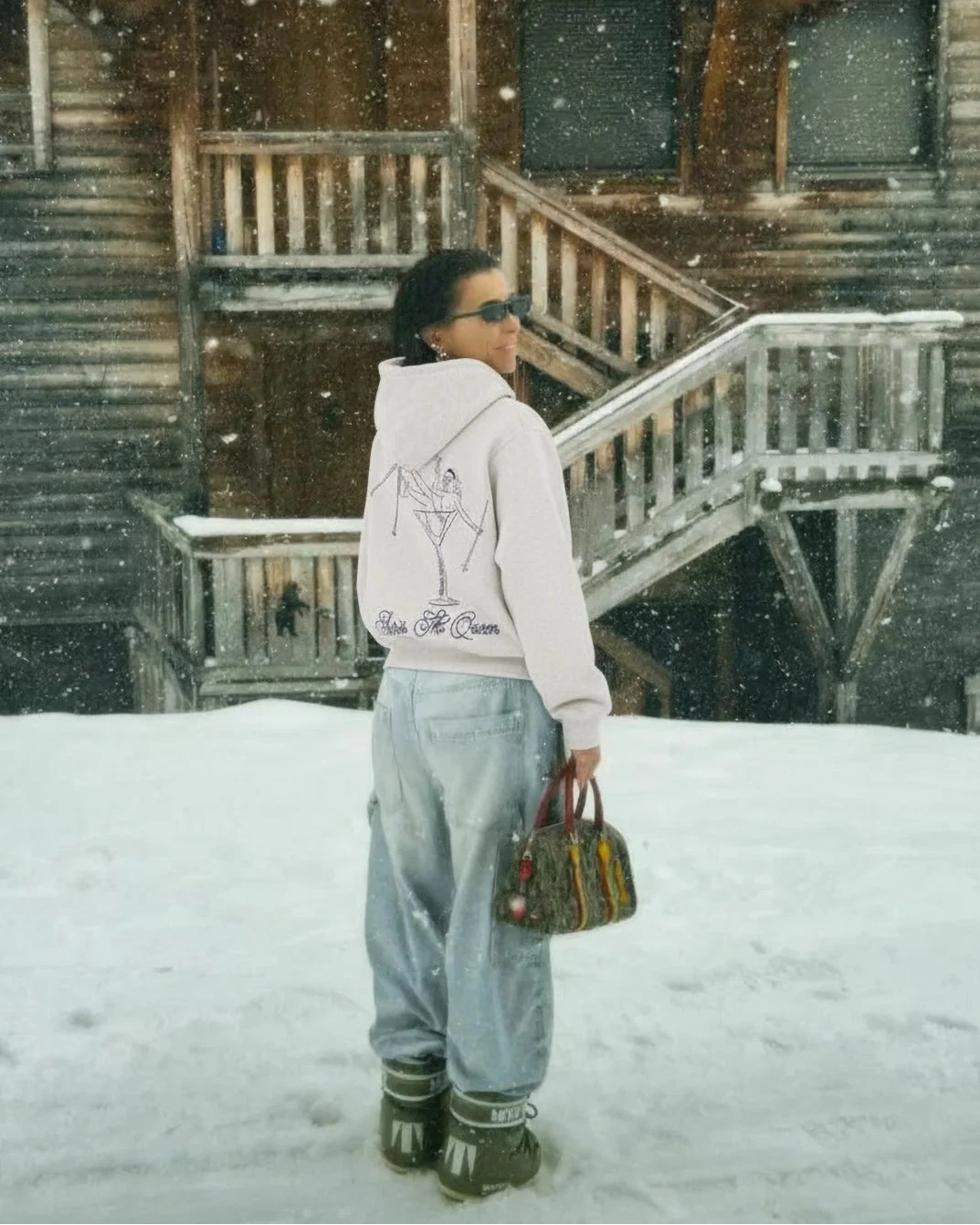 Person standing in front of a wooden cabin during a snowfall