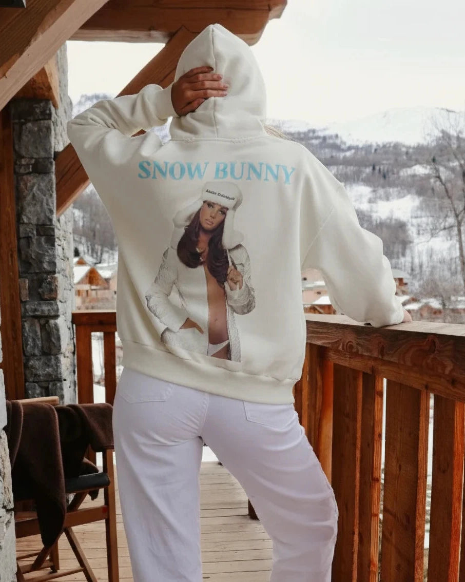 Person wearing a hoodie with a graphic design on a wooden deck with stone walls.