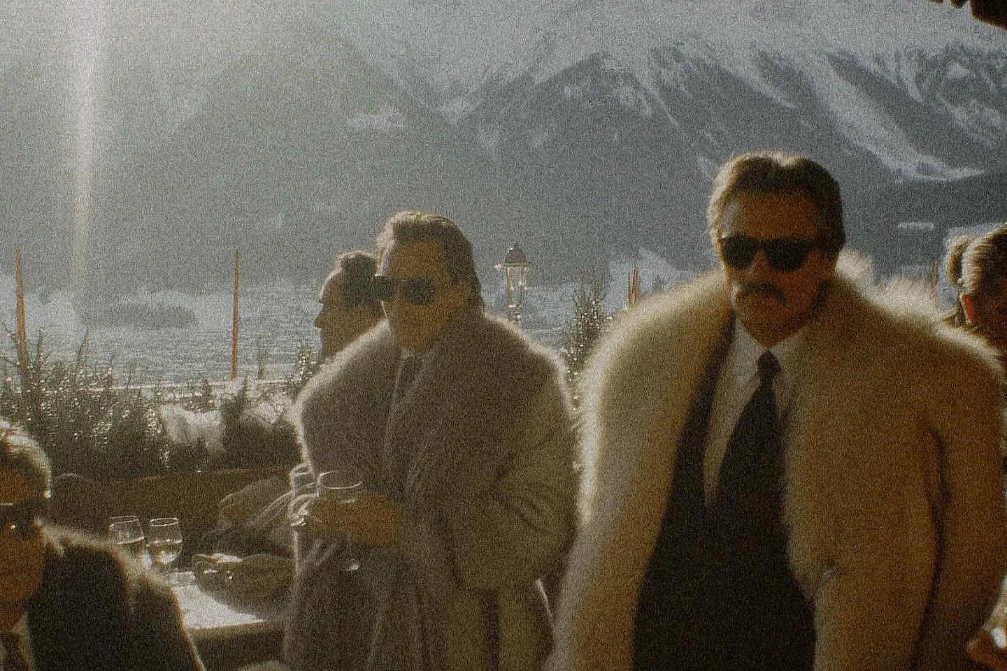 Two men in fur coats standing outdoors with mountains in the background