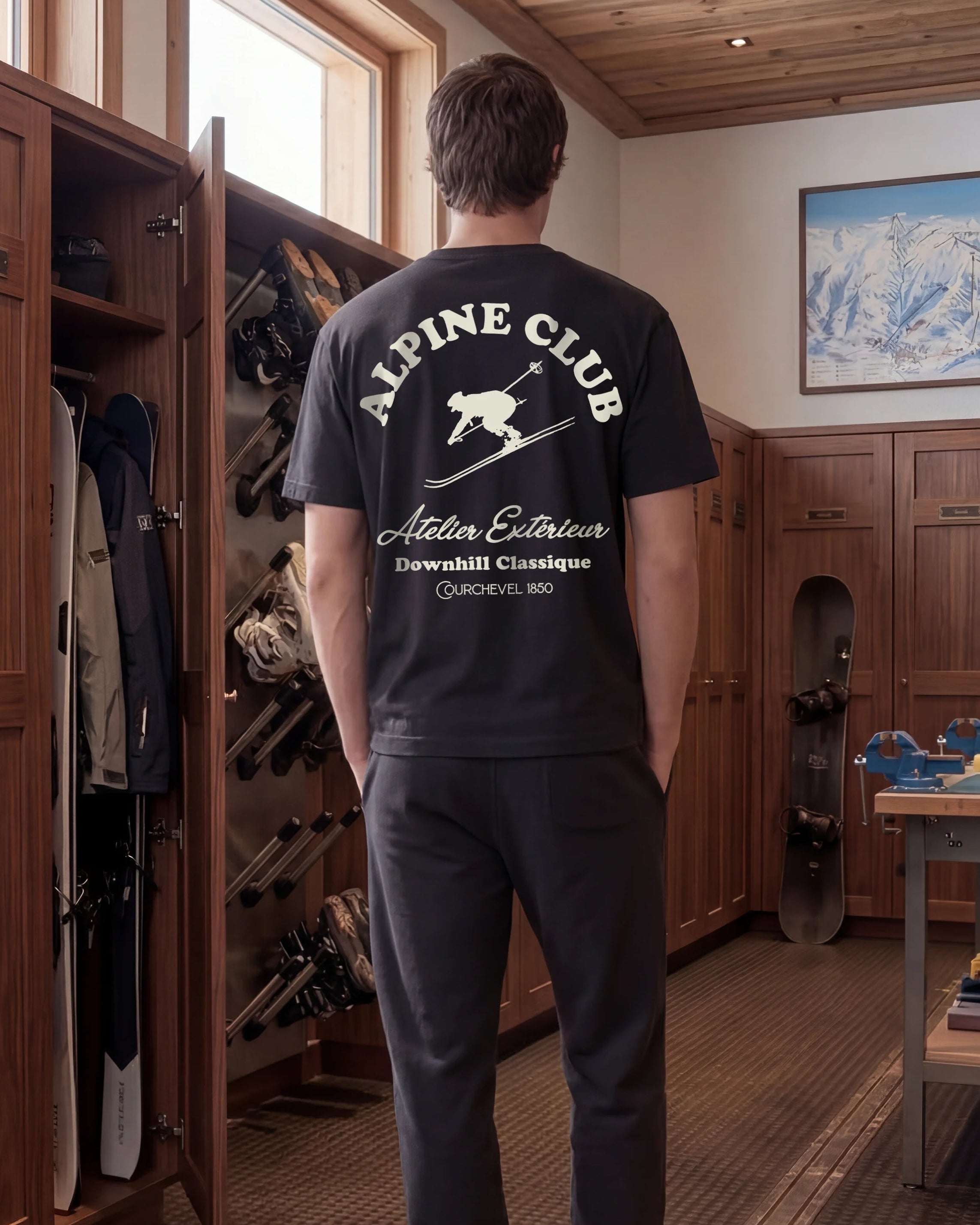 Person wearing an 'Alpine Club' t-shirt in a room with wooden cabinets and ski equipment.