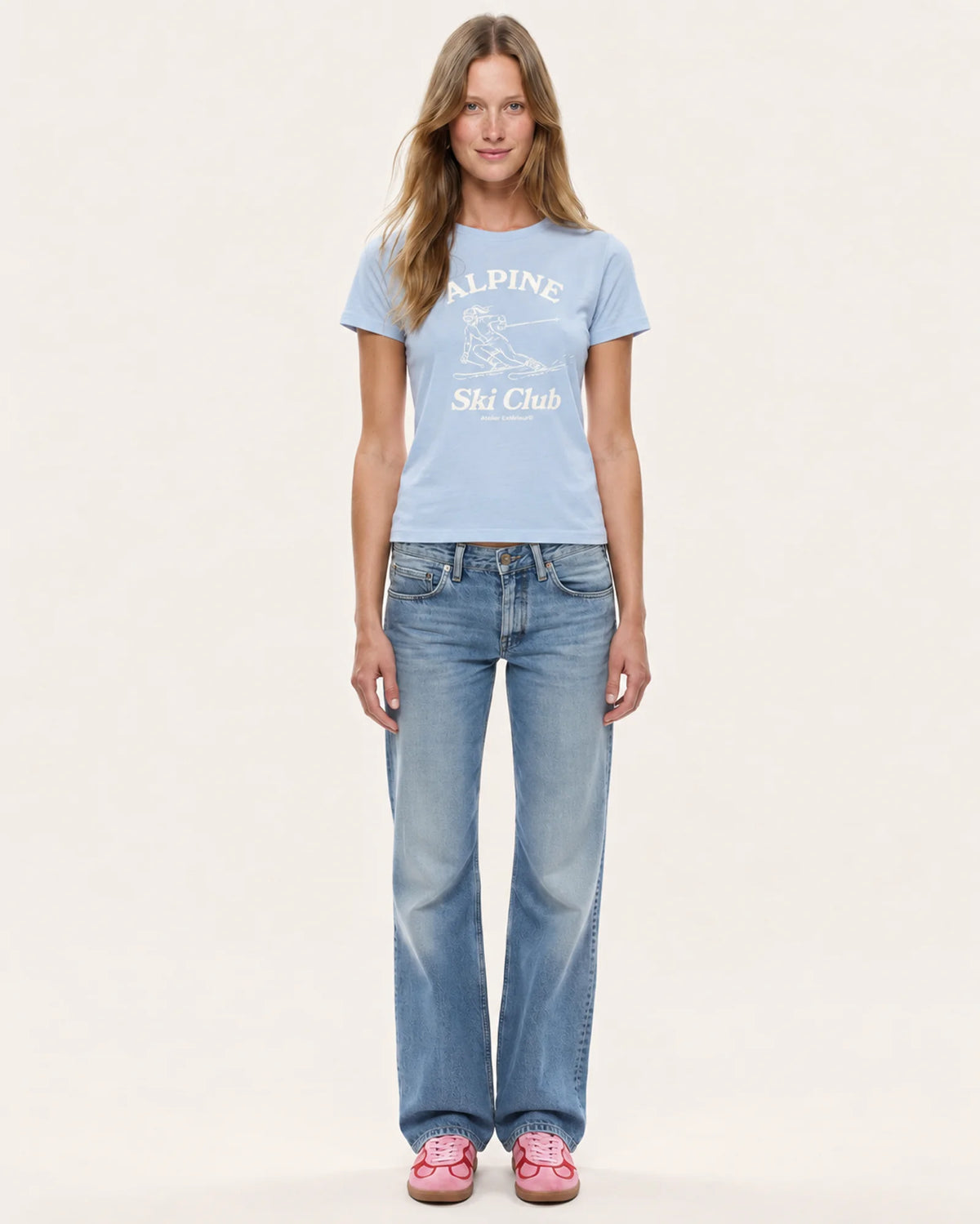 Model wearing the Alpine Ski Club women's tee in baby blue with straight-leg jeans, front view