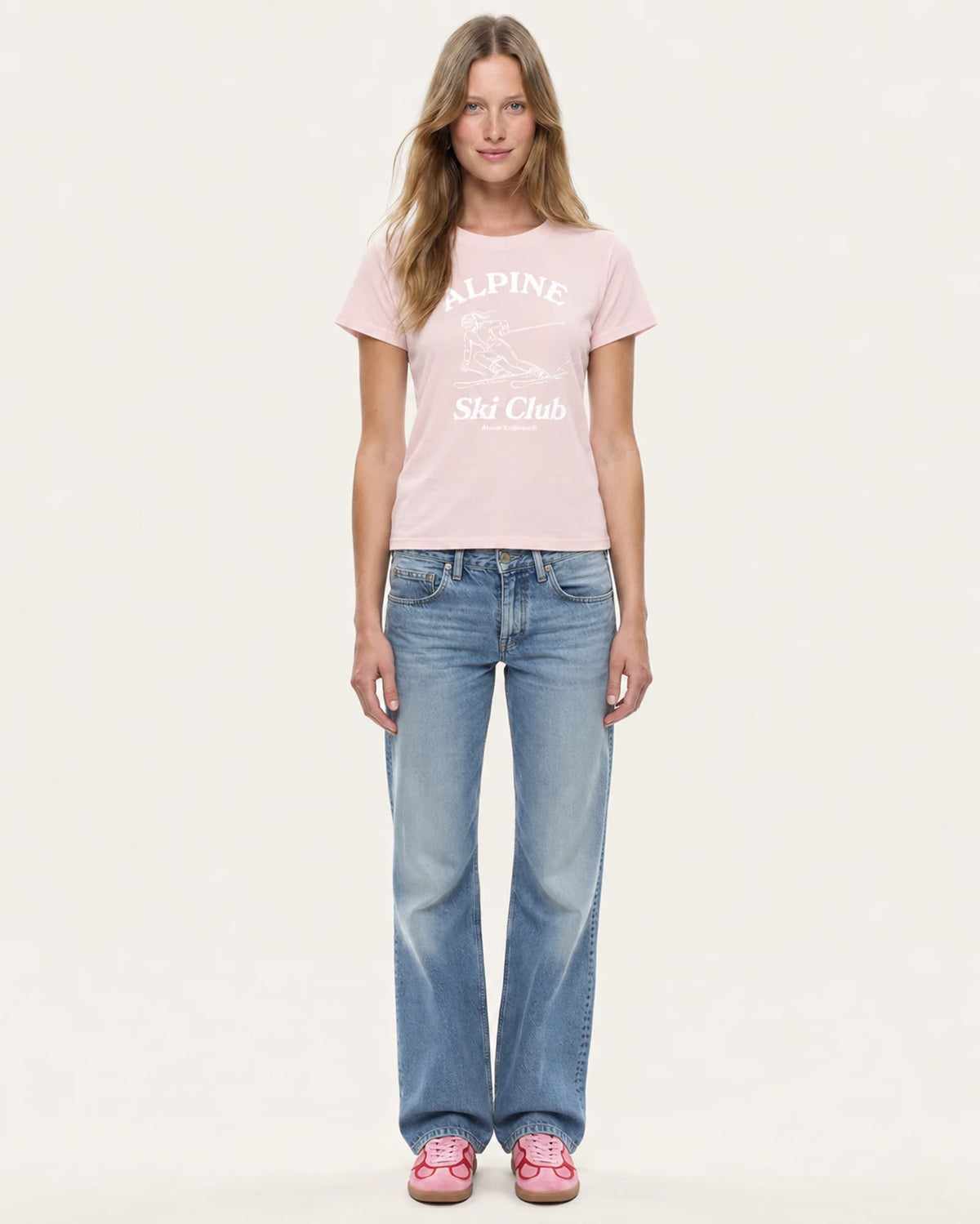 Model wearing the Alpine Ski Club women's tee in pink with straight-leg jeans, front view