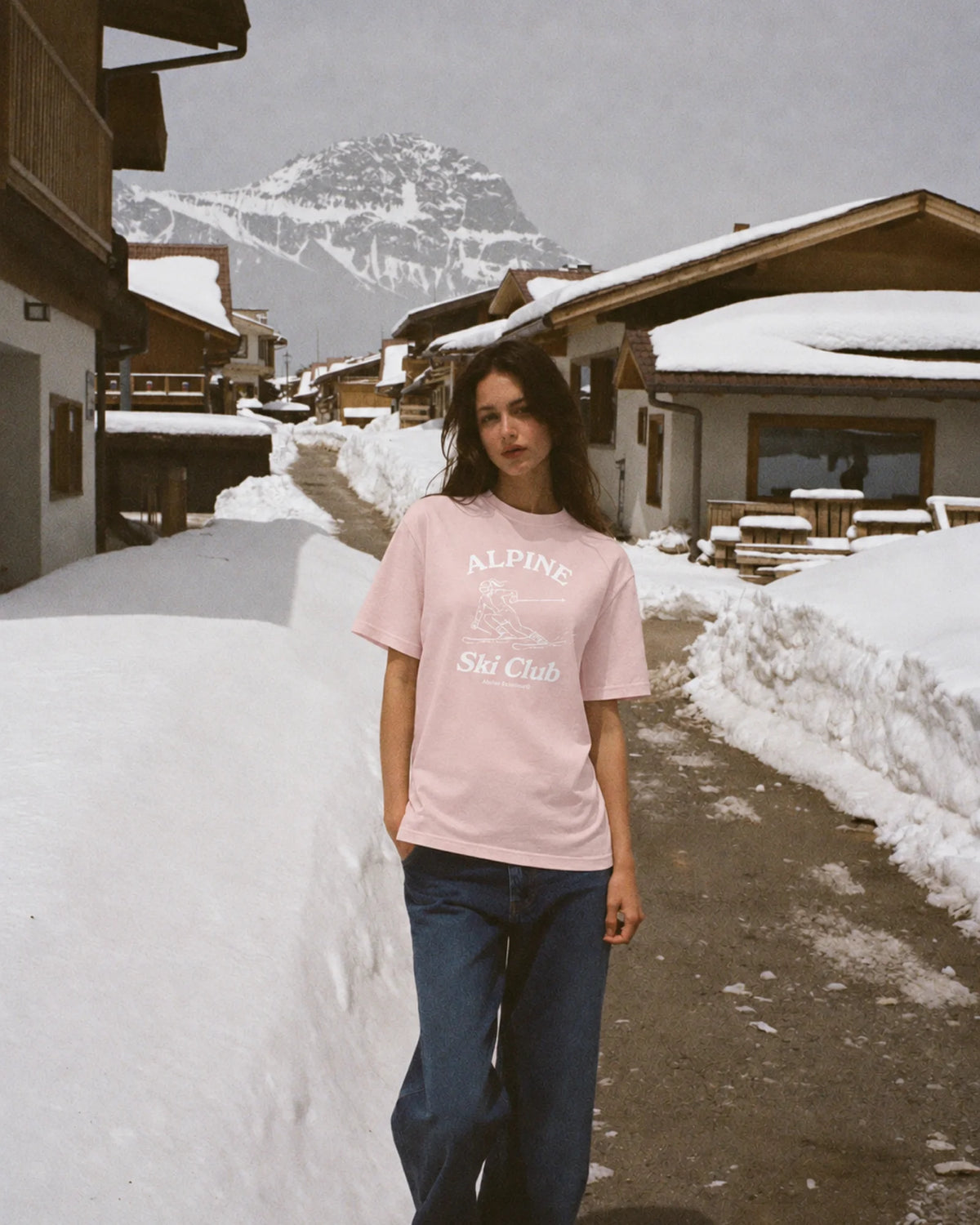 Woman wearing the pink Alpine Ski Club tee on a snowy village street in the Alps