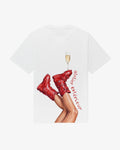 Champagne women's tee in white, back view, red ski boots with a champagne flute balanced on the toe
