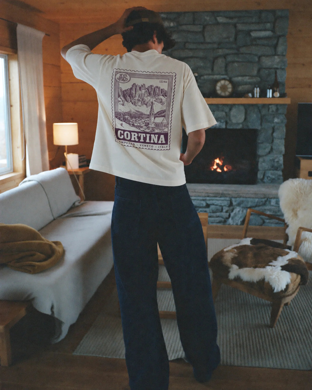 Man wearing the ecru Cortina tee outdoors, showing the resort stamp back print