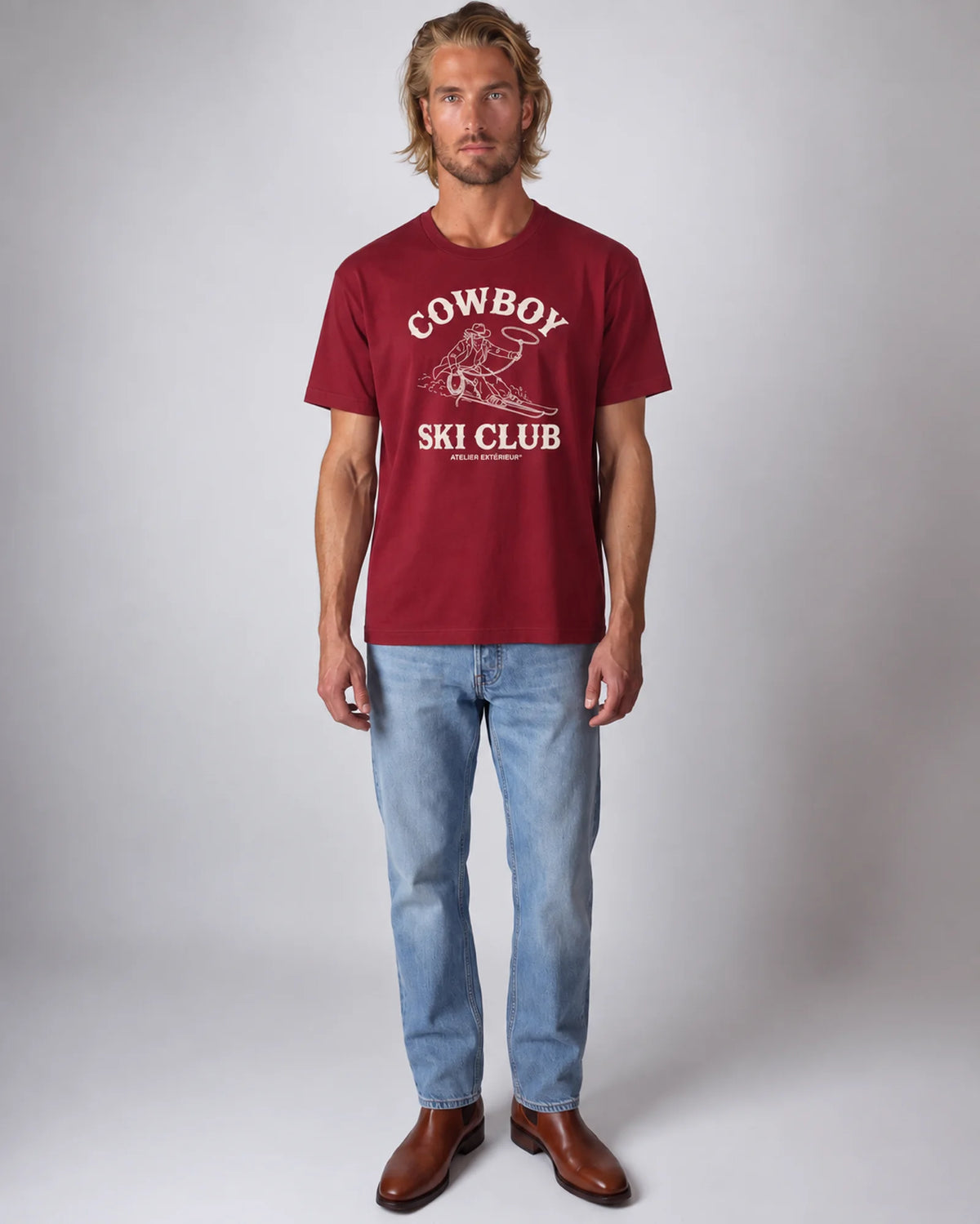 Model wearing the red Cowboy Ski Club tee in a studio, front view
