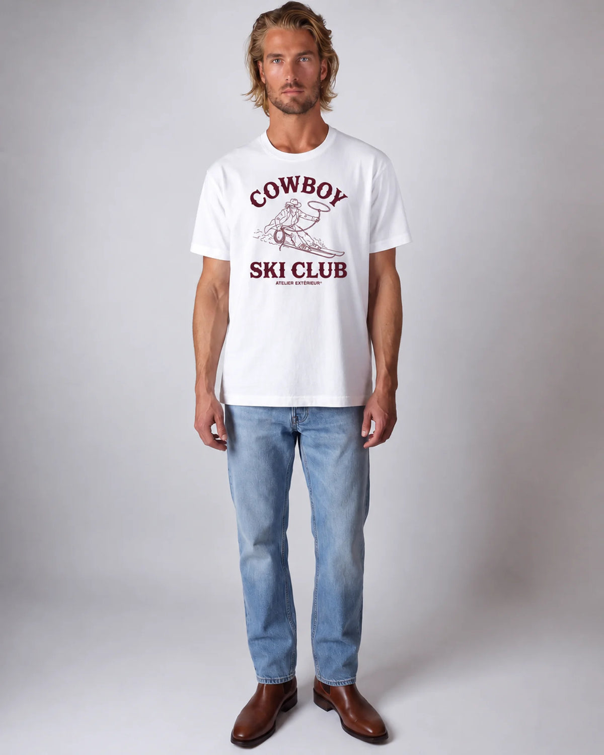 Model wearing the white Cowboy Ski Club tee in a studio, front view