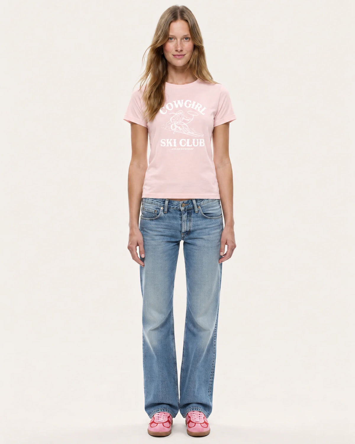 Model wearing the Cowgirl Ski Club women's tee in pink with straight-leg jeans, front view