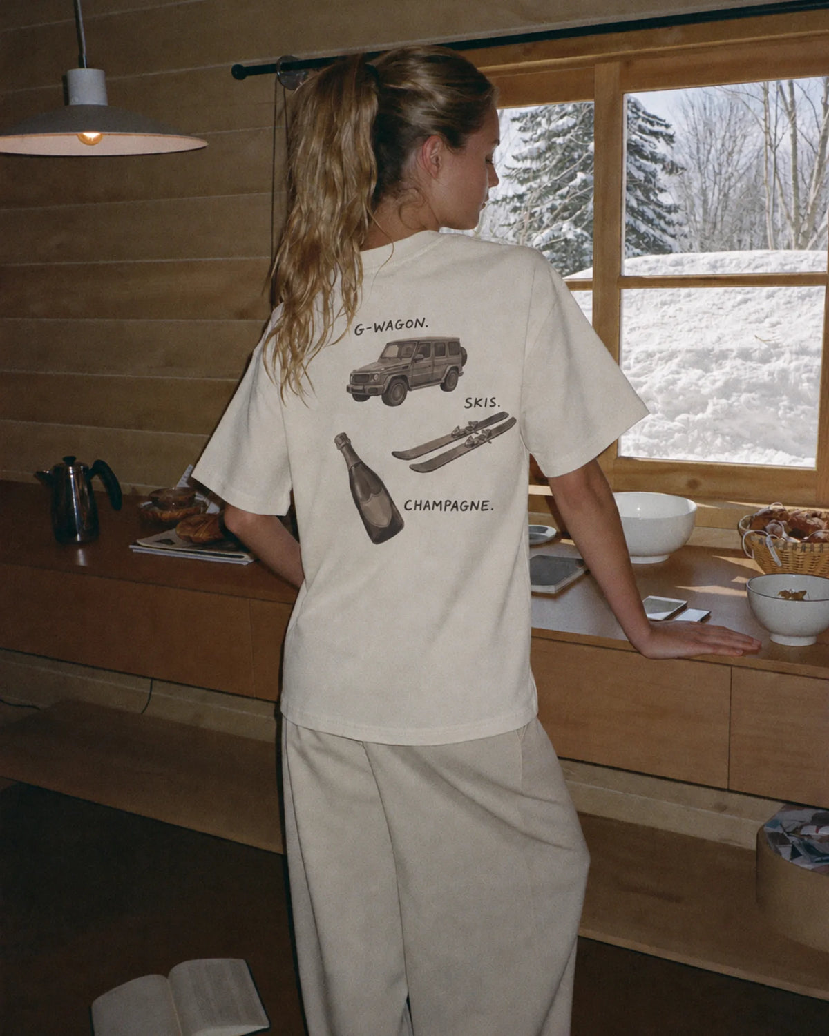 Woman wearing the ecru Essentials tee outdoors, showing the hand-painted back print