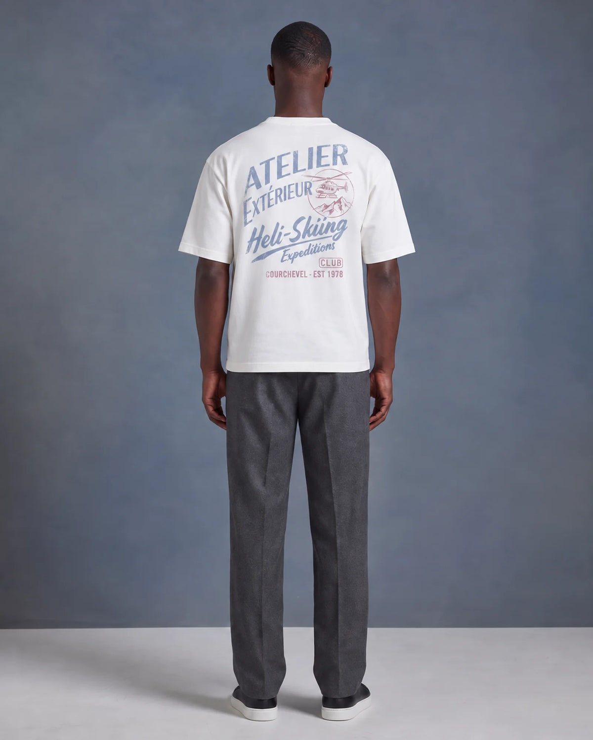 Model wearing the white Heli Skiing tee in a studio, back view