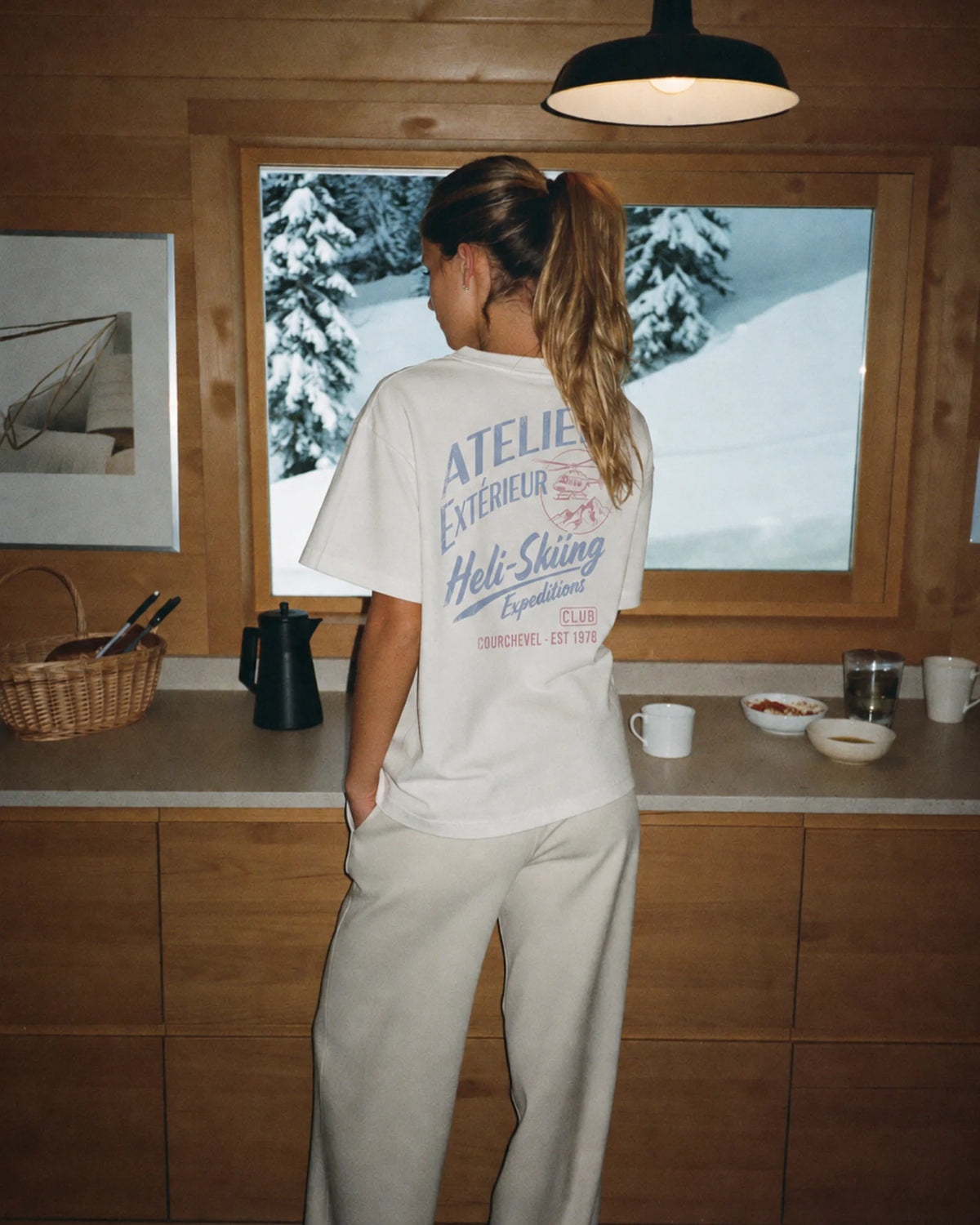 Woman wearing the white Heli Skiing tee outdoors, showing the back print