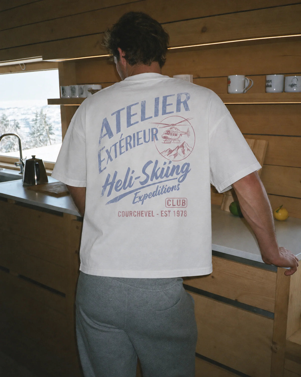 Man wearing the white Heli Skiing tee outdoors, showing the back print