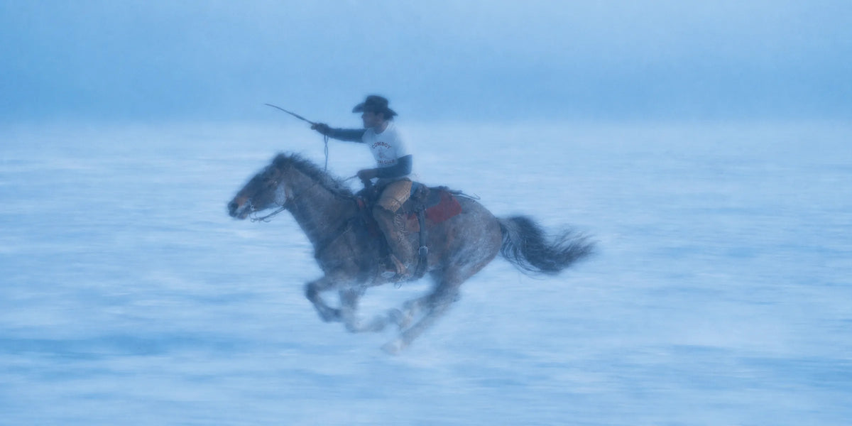 Cowboy riding a galloping horse across the snow