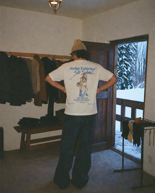 Man wearing the ecru Julia tee outdoors, showing the Ski School back print