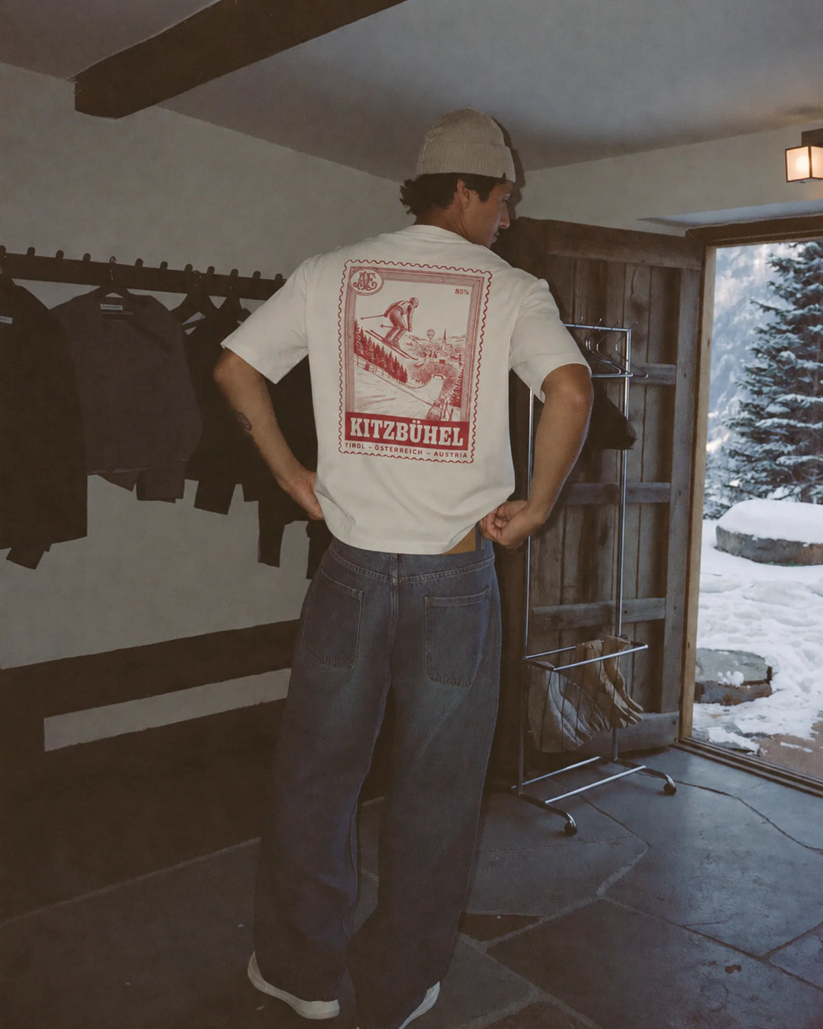 Man wearing the ecru Kitzbühel tee outdoors, showing the resort stamp back print