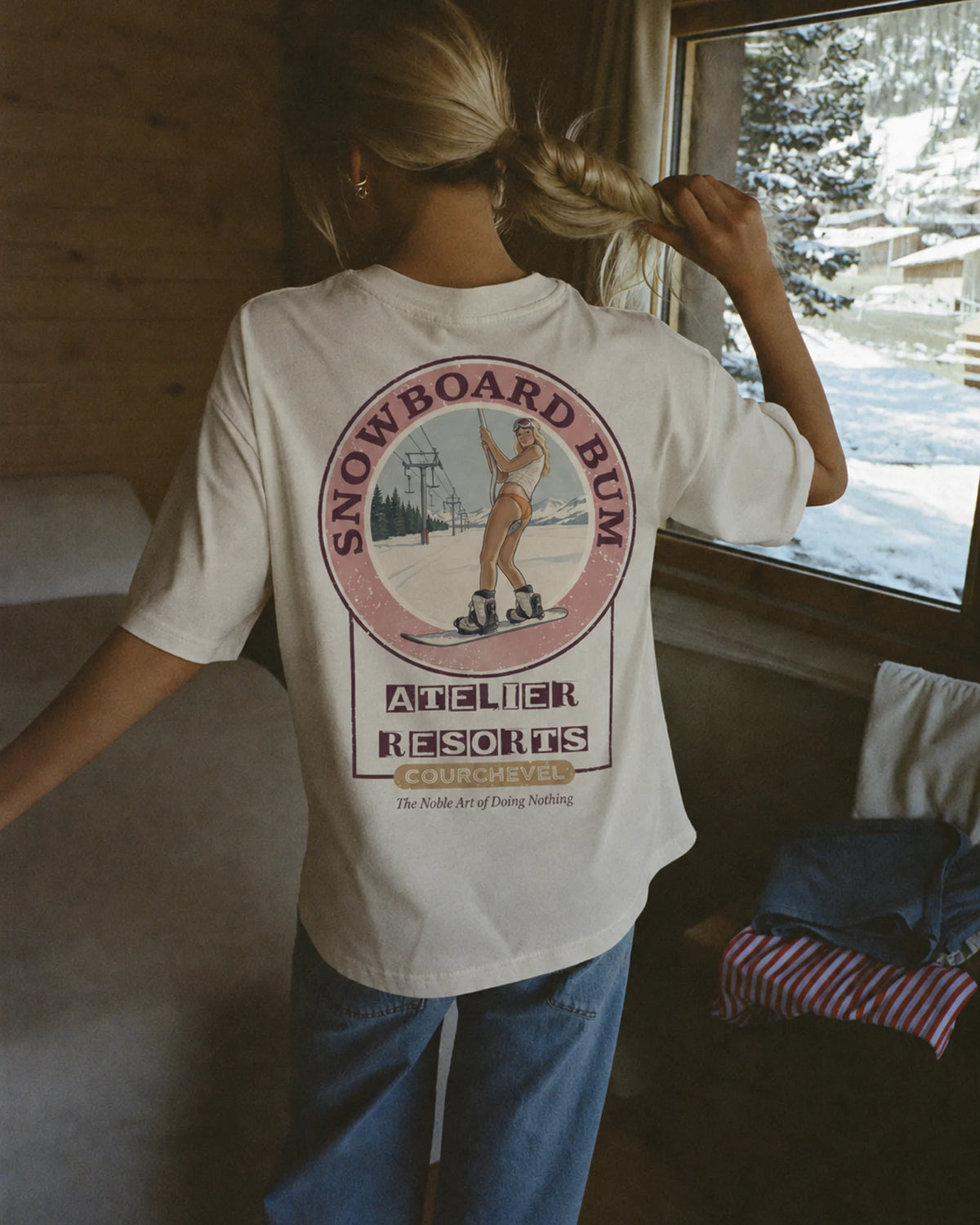 Woman wearing the ecru Snowboard Bum tee in the snow, back print visible