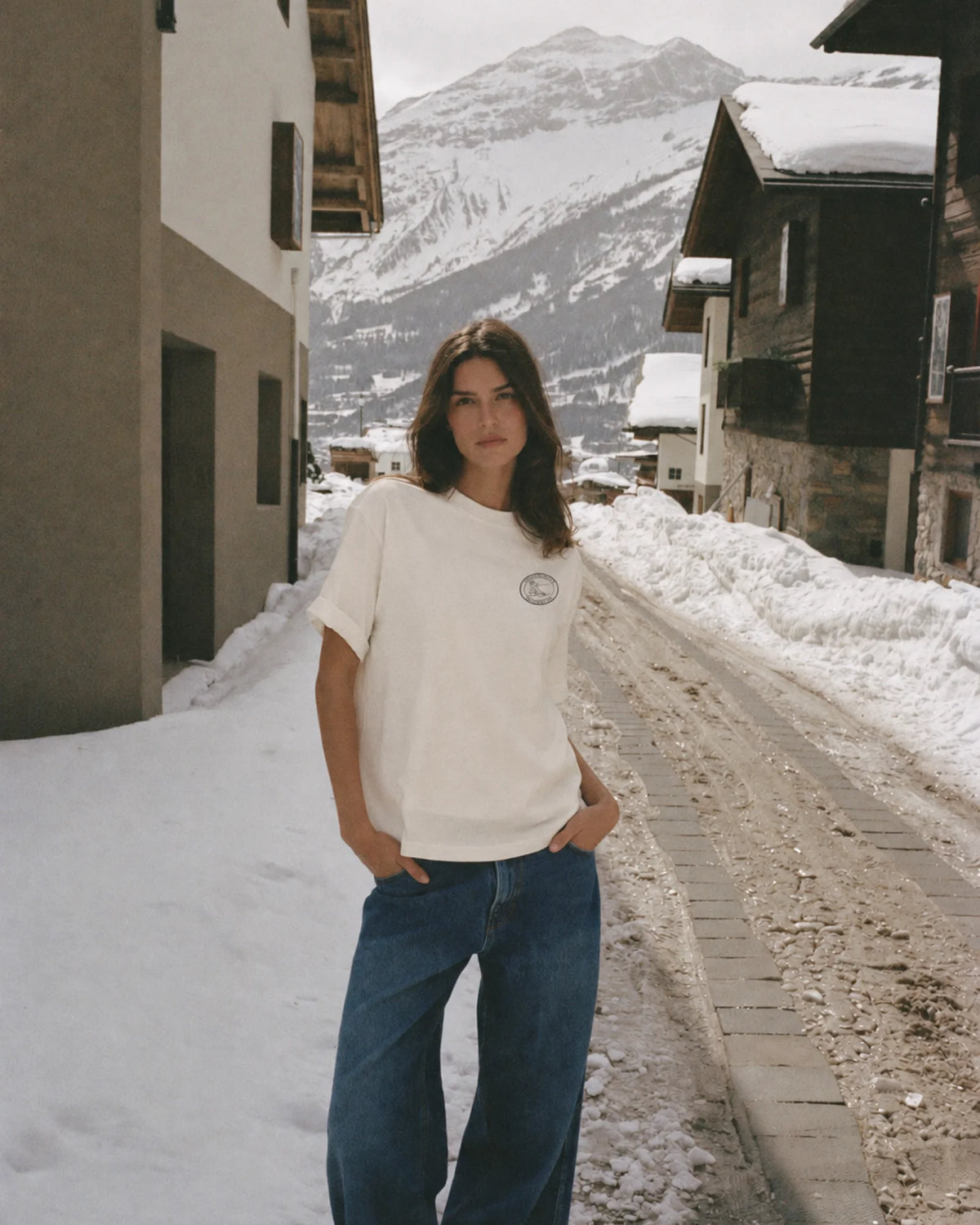 Woman wearing the ecru Ski Club tee with jeans on a snowy village street in the Alps