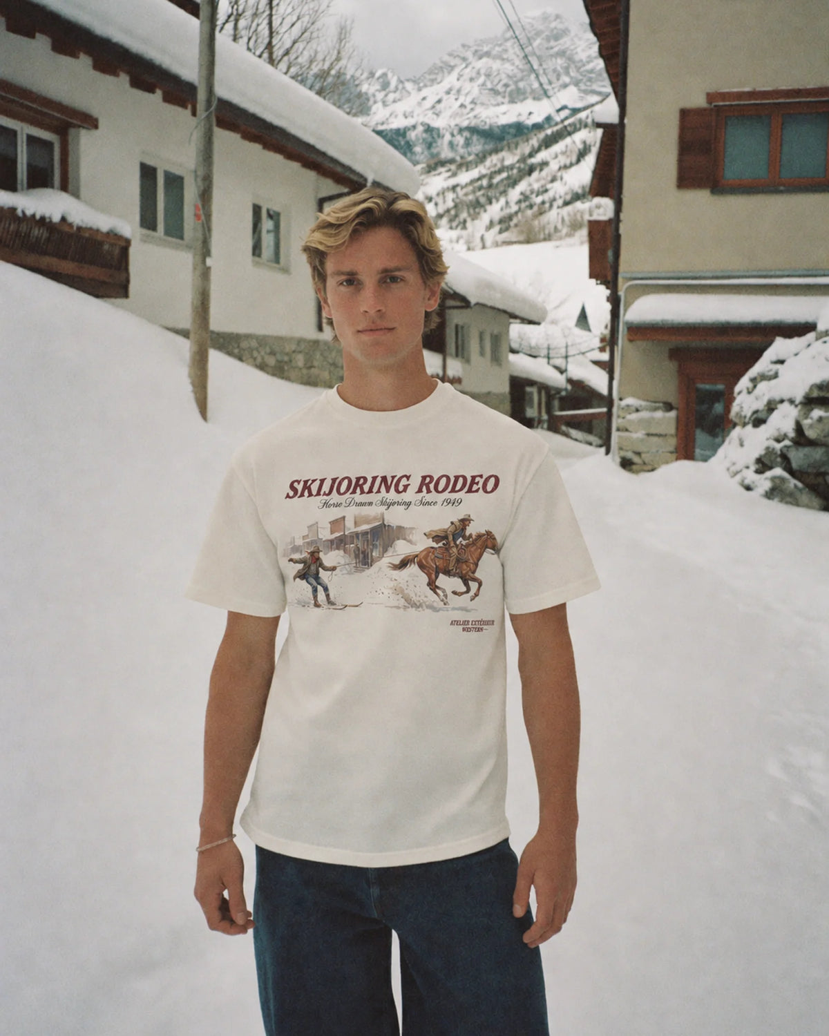 Man wearing the ecru Skijoring tee in the snow, front print visible