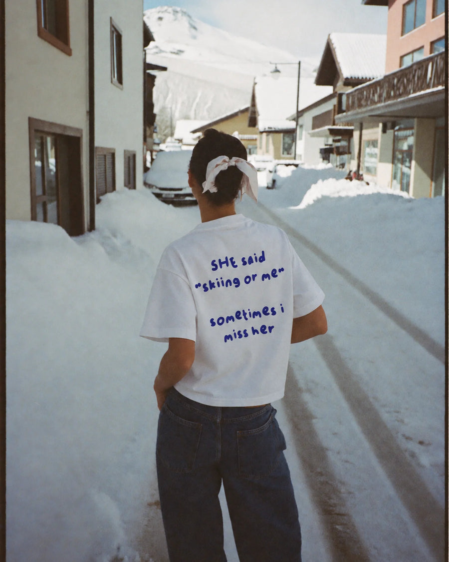 Woman wearing the white Skiing or Me tee in the snow, back print visible
